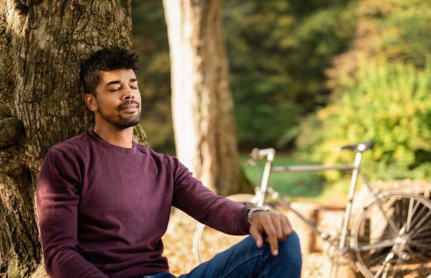 Man sitting against a tree with his eyes closed.