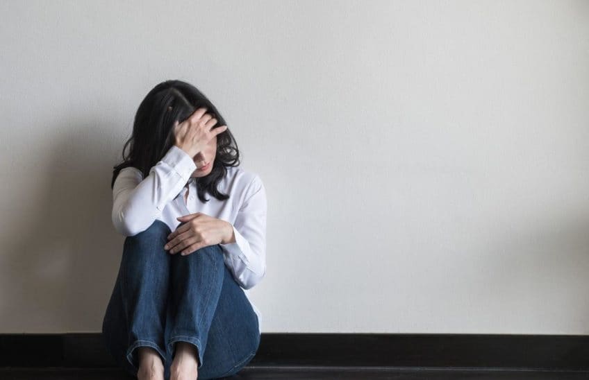 Woman sitting on the floor and holding her hand to her forehead.