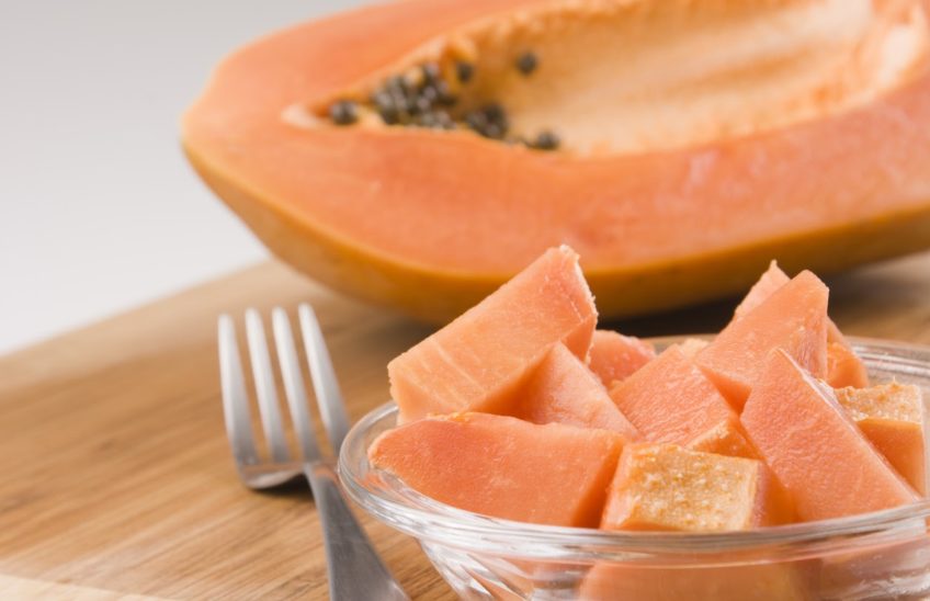 chunks of papaya in a bowl in front of a half papaya on a wooden cutting board.