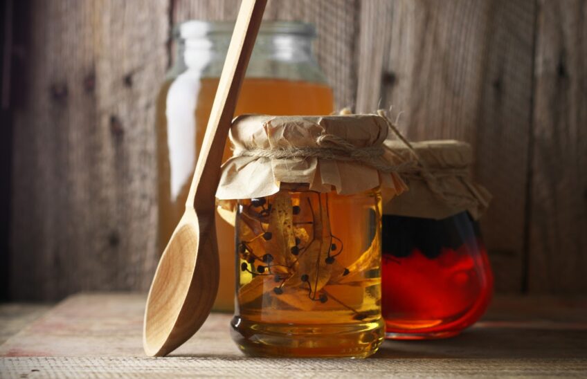 Wooden spoon leaning on a jar of honey with herbs in it.