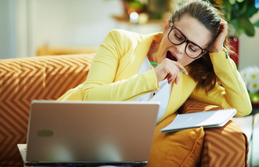 Woman with a laptop slouching over and yawning.