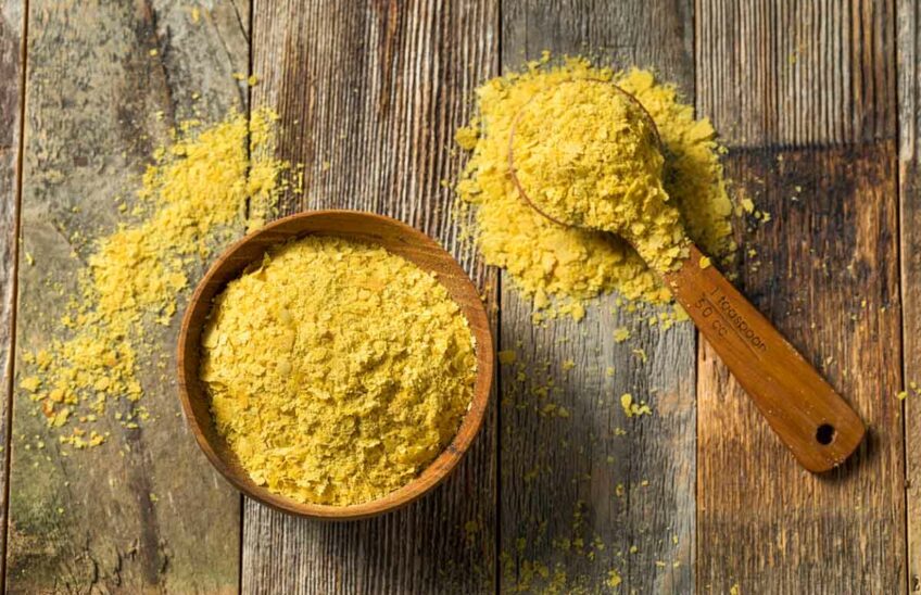 Nutritional yeast in a bowl and a spoon on a wood surface