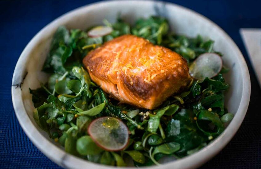A bowl of leafy greens with cooked salmon