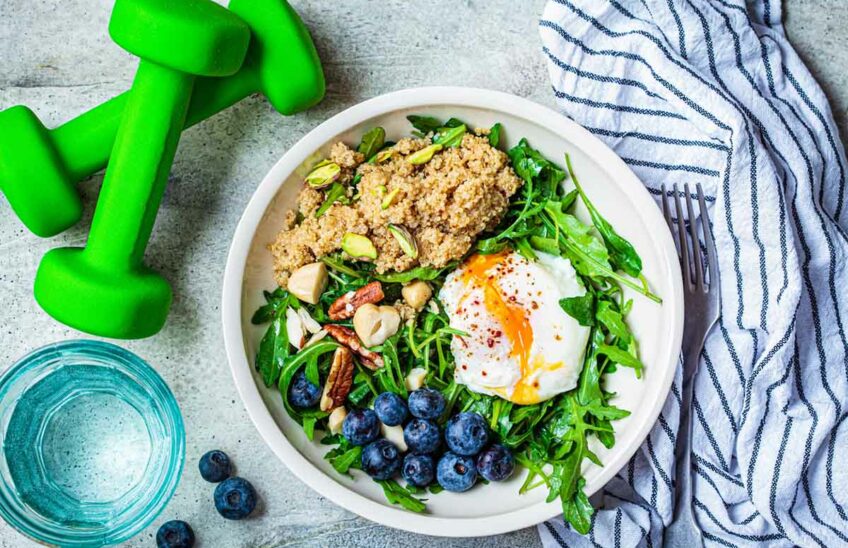 Quinoa salad with berries, poached egg and nuts, next to two dumbbells