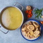 A pot of broth next to cooked bones and fresh vegetables
