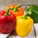 Yellow, red, green, and orange bell peppers on a wood surface