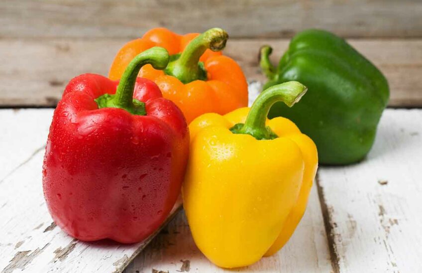 Yellow, red, green, and orange bell peppers on a wood surface