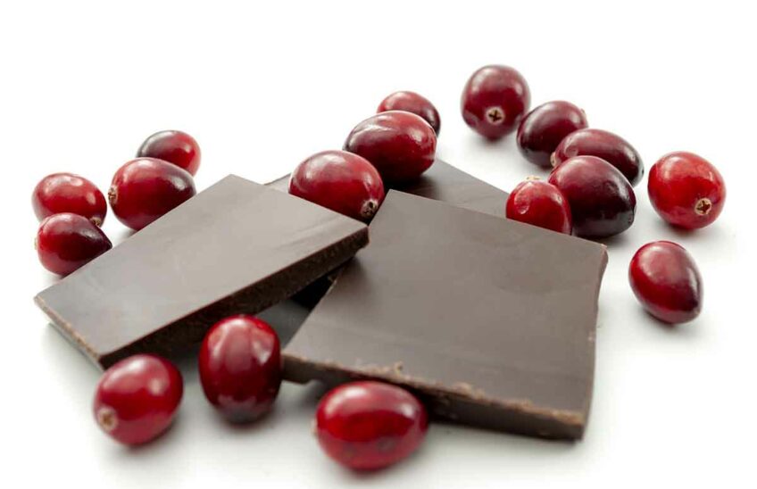 Fresh cranberries and pieces of dark chocolate on a white surface